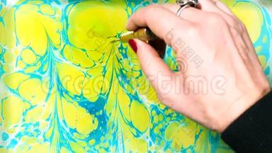 埃布鲁是在液态水面上作画的艺术。 纸大理石花纹。 女人用刷子、黄色和蓝色油漆画画。 关闭